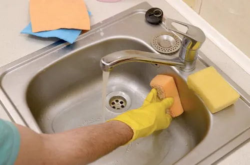 Scrubbing a stainless steel kitchen sink during a deep clean